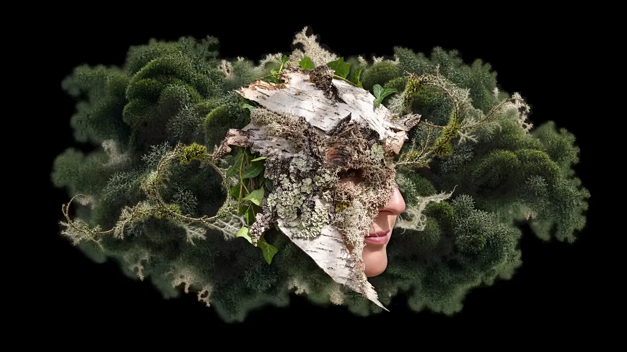 Le visage de Hilbi sous un masque d’écorce, de lichen et de mousse